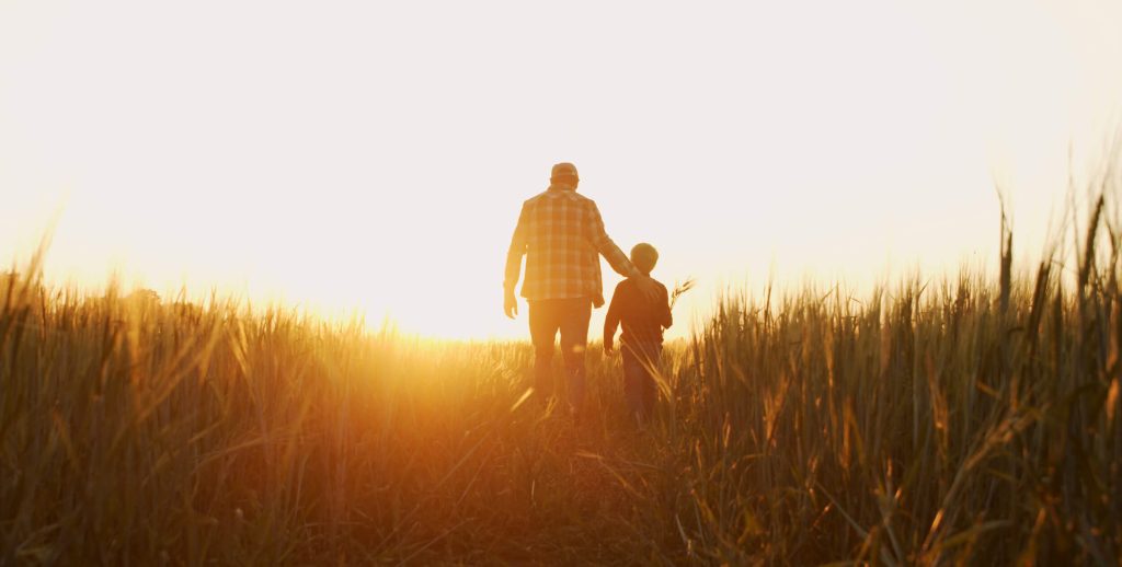 Person and child walking through the grass at sunrise.